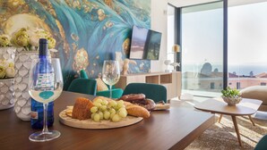 A dining table with a bottle of wine, a glass, grapes, and pastries, a painting on the wall, and a view through a large window. - 200m NEW A Villa with private, heated pool and amazing ocean view (Costa Adeje)