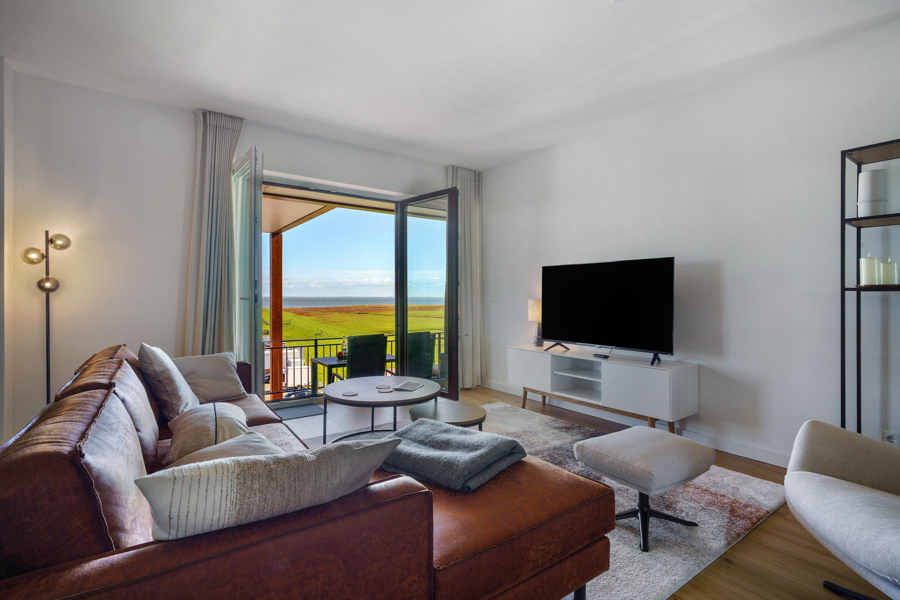 Ein modernes Wohnzimmer mit großem Fernseher, einer Couch, einem Couchtisch und Blick auf die Landschaft durch eine Glastür.