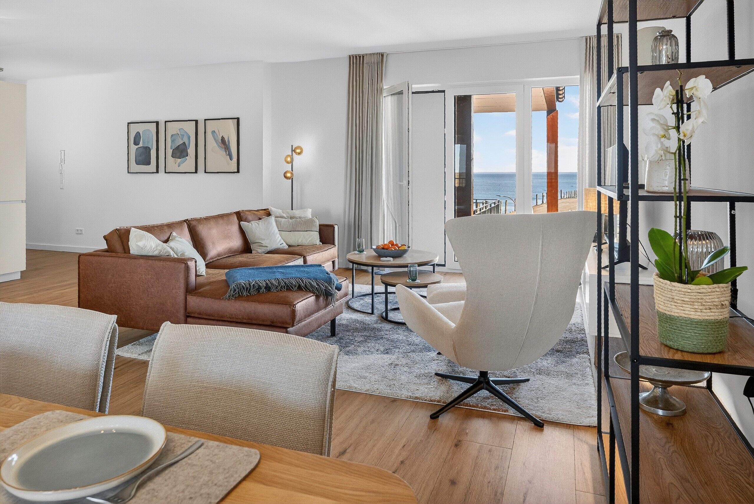A modern living room with a brown leather sofa, a white armchair, and a dining area with a table and chairs.