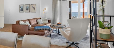 Ein modernes Wohnzimmer mit einem braunen Ledersofa, einem weißen Sessel und einem Essbereich mit Tisch und Stühlen.