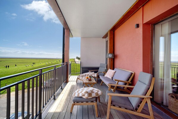 Ein Balkon mit Blick auf ein grünes Feld und Schafe, ausgestattet mit zwei Stühlen und einem kleinen Tisch.