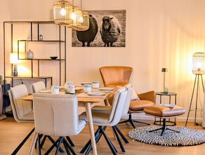 A dining area with a wooden table, chairs, and a modern pendant light fixture. - Apartment “Bodil” with Sea View, Balcony, and Wi-Fi (Pellworm)