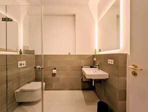 Ein modernes Badezimmer mit Duschkabine aus Glas, Toilette, Waschbecken und Spiegel.
