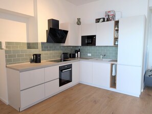 Moderni keittiö, jossa on valkoiset kaapit, sisäänrakennettu uuni, mikroaaltouuni ja kahvinkeitin.