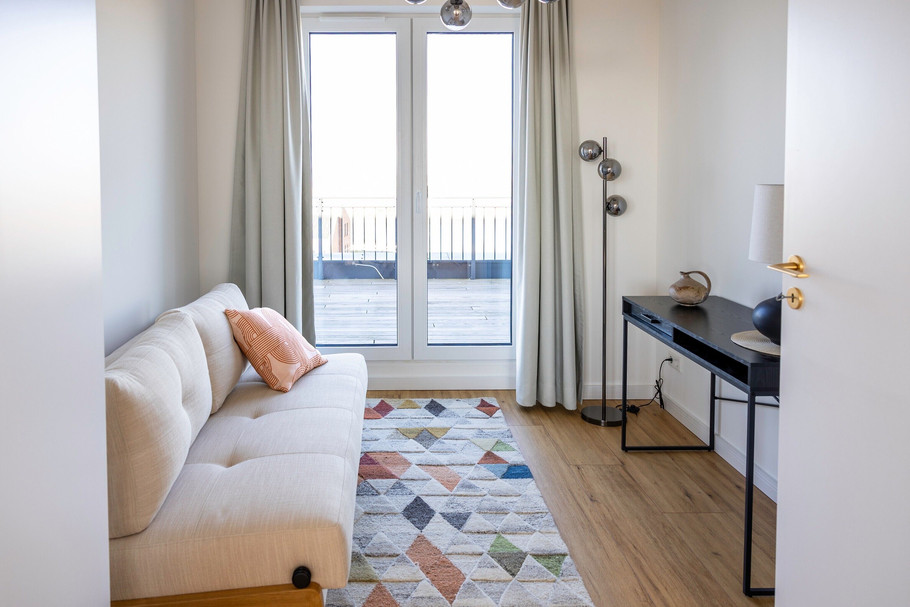 Et moderne værelse med sofa, skrivebord og udsigt gennem et stort vindue.