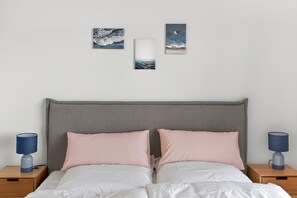 A bedroom with a grey headboard, two pink pillows, white bedding, and two bedside tables with lamps. - Penthouse 'Smilla' with Sea View and Wi-Fi (Pellworm)
