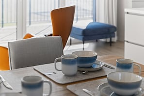 A dining area with a table set for two, featuring a blue and white mug, a white mug, and a blue and white bowl. - Penthouse 'Smilla' with Sea View and Wi-Fi (Pellworm)