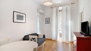 Een kamer met een eettafel, een bank, een tv op een meubel en een raam met gordijnen.