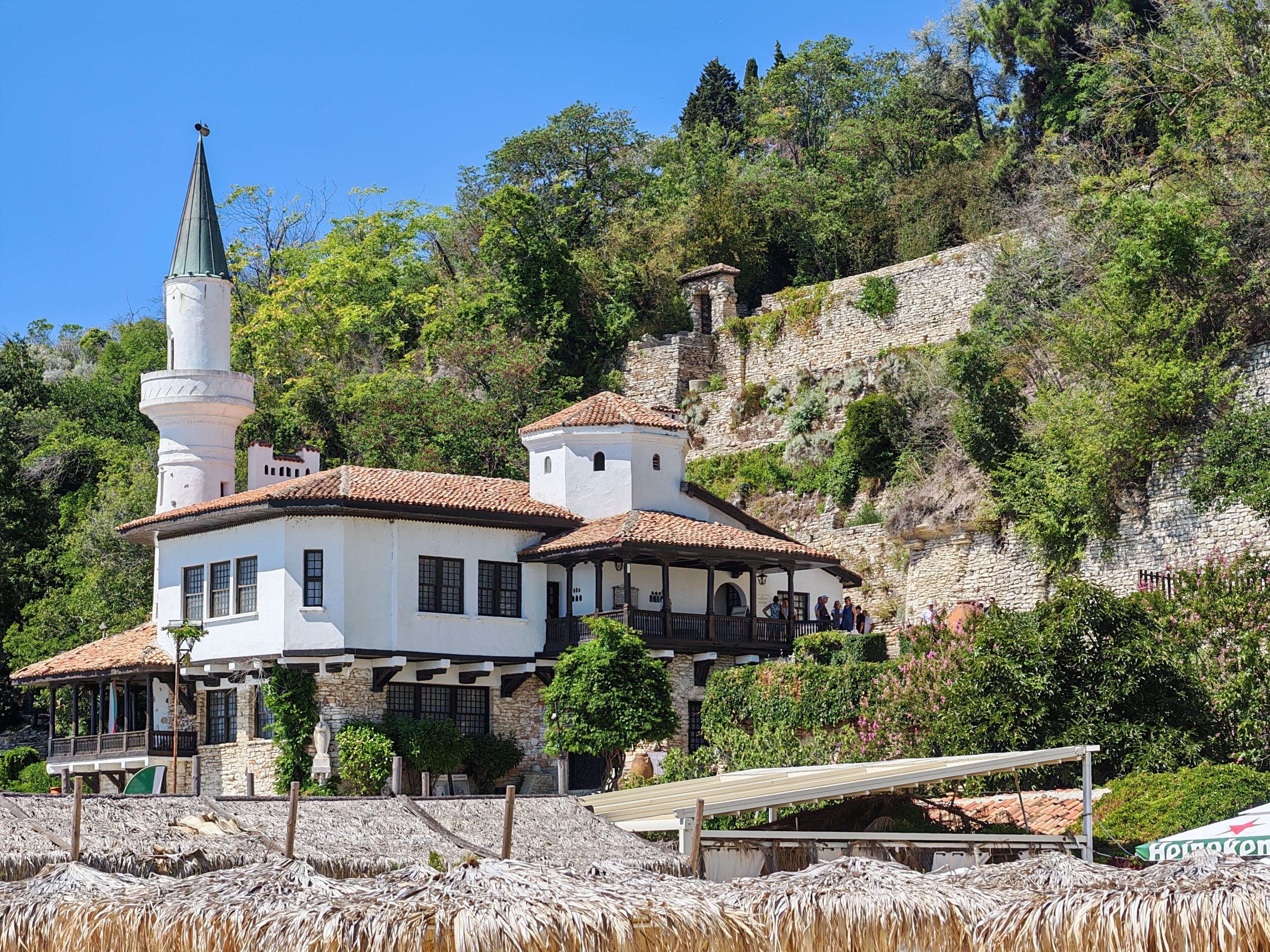 A white building with a tower, surrounded by greenery and stone walls.