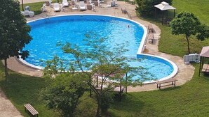 A large outdoor swimming pool surrounded by lounge chairs and umbrellas, with a building in the background. - Ines - Golf and the Sea in Bulgaria (Balchik)