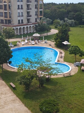 Una amplia piscina al aire libre rodeada de tumbonas y sombrillas, con un edificio al fondo.