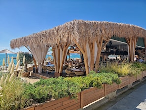 Ein Restaurant am Strand mit Außenbereich, einem Reetdach und Meerblick.