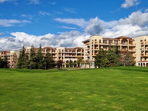 A multi-story hotel with balconies, a green lawn, and a clear sky.