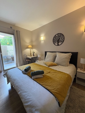 A hotel room with a bed, a table with a lamp, a chair, and a view of the outdoors. - Apartment & TerraceS t-Rémy Conciergerie Maurin (SAINT REMY DE PROVENCE)