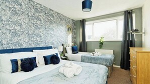 Habitación de hotel con dos camas, un aparador, una ventana con cortinas y una pared con diseño tipo mármol.