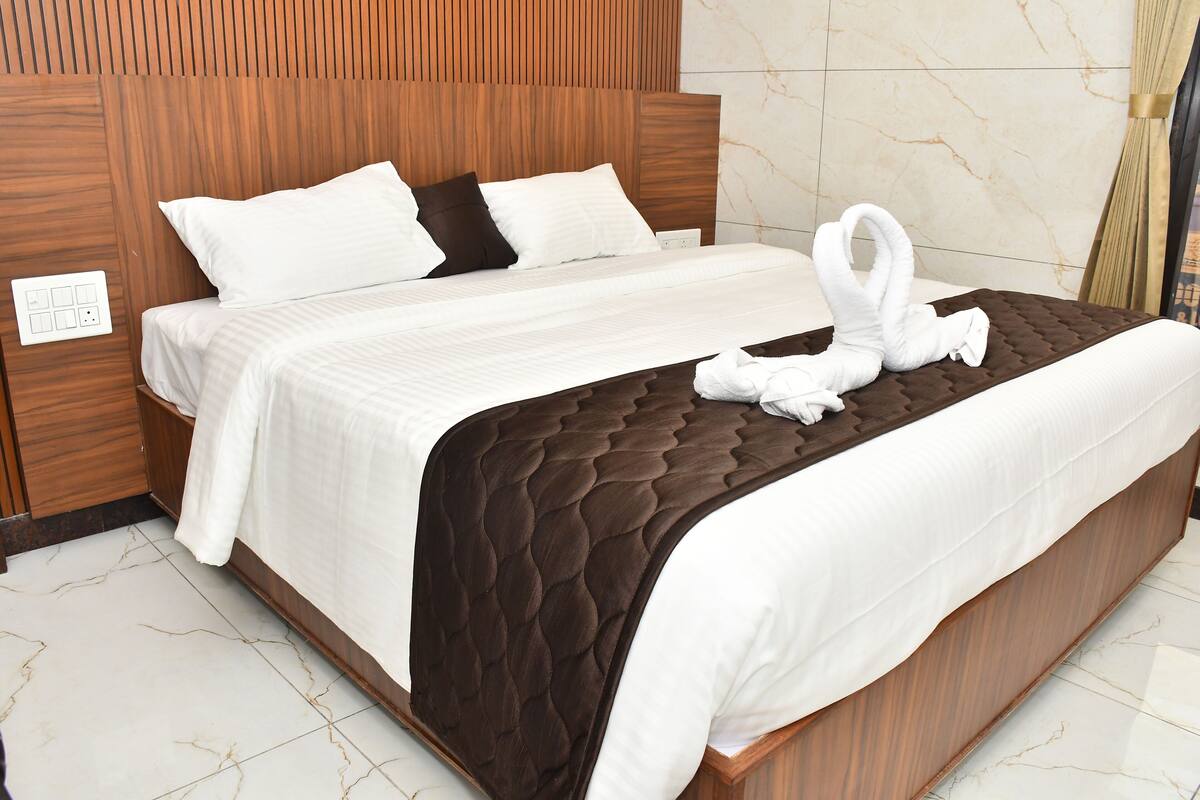 A neatly made bed with a brown quilt, white bedding, and two white towels arranged in a swan shape on the bed.