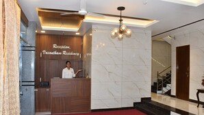 A reception area with a receptionist, a marble wall, a red carpet, and a staircase. - Vasantham Residency (Rameshwaram)