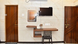 A room with a wooden desk, a television, a coffee maker, and a patterned chair. - Vasantham Residency (Rameshwaram)
