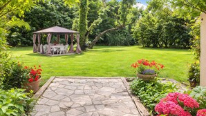 A stone patio leading to a gazebo with a table and chairs, surrounded by lush greenery and flowering plants. - Sweet Pea sunny cottage in Vence with pool garden private parking (Vence)