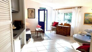 A living room with a sofa, a chair, a wooden cabinet, a small table with flowers, and a window with curtains. - Sweet Pea sunny cottage in Vence with pool garden private parking (Vence)