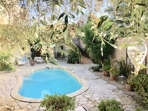 A swimming pool surrounded by stone tiles, with a patio area and potted plants.