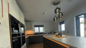 A modern kitchen with built-in appliances, a central island, pendant lighting, and large windows.