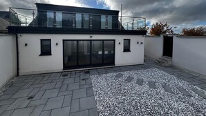 A modern building with a glass balcony, a flat roof, and a paved courtyard.