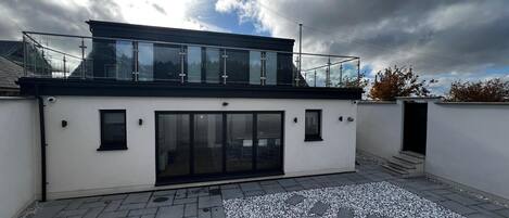 A modern building with a glass balcony, a flat roof, and a paved courtyard.