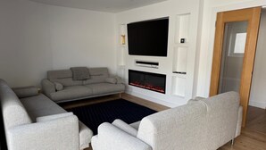 A modern living room with a grey sofa, a flat-screen TV, a fireplace, and a wooden floor. - 5 Bed House/sleeps10/free Parking/pets/city Centre (Edinburgh)