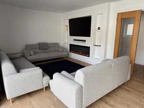 A modern living room with a grey sofa, a flat-screen TV, a fireplace, and a wooden floor. - 5 Bed House/sleeps10/free Parking/pets/city Centre (Edinburgh)