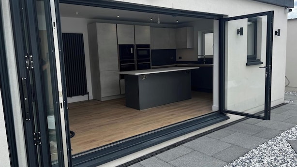 A modern kitchen with a central island, built-in appliances, and a sliding glass door entrance.