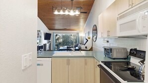 Una cocina moderna con techo de madera, armarios blancos, microondas, tostadora y un lavamanos.