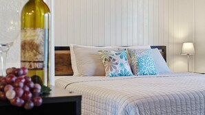 Una cama bien hecha con almohadillas estampadas, una botella de vino y una copa sobre una mesita de noche.