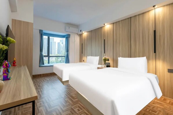 A hotel room with two beds, a wooden wall panel, a window with a view, and a desk with a vase of flowers. - City Bang Qingshe Hotel (Longhua Guanlan Hi-Tech Science Park Shop) (Shenzhen)