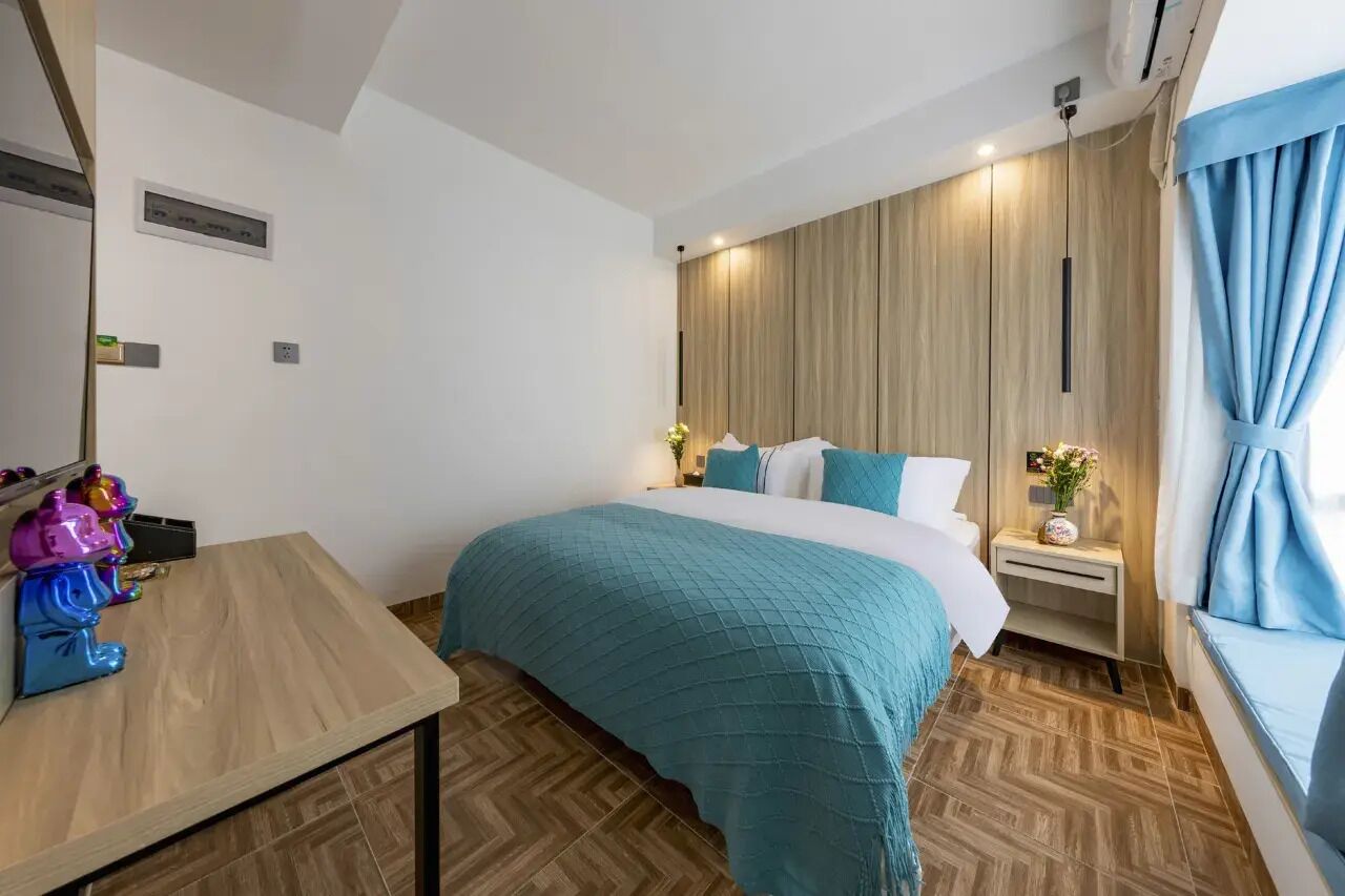 A hotel room with a bed, bedside table, and a window with curtains.