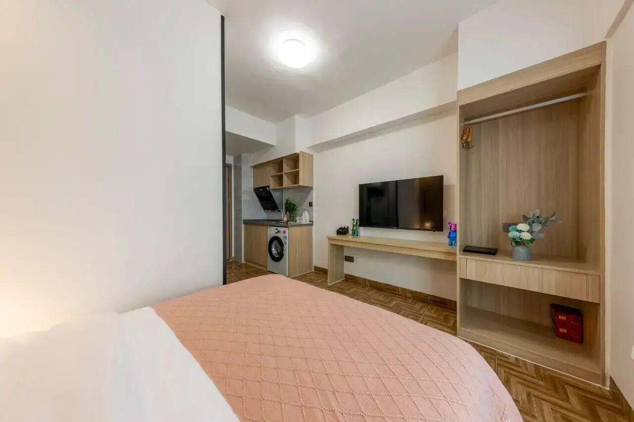 A bedroom with a bed, a TV, a wardrobe, and a washing machine in the background.