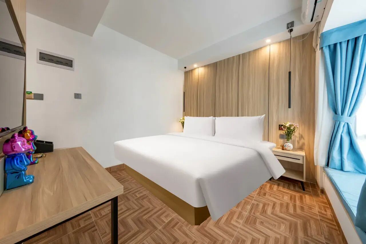 A hotel room with a bed, bedside table, and a window with curtains.