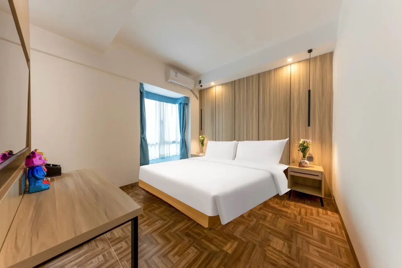 A modern hotel room with a bed, bedside table, nightstand, and a window with curtains.