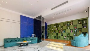 Un hall d’entrée moderne avec un canapé vert, un mur d’accent bleu, une bibliothèque verte et un sol en marbre.