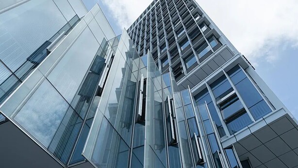 Un immeuble moderne de grande hauteur, doté de façades en verre réfléchissant et d’une structure de fenêtres en forme de grille.