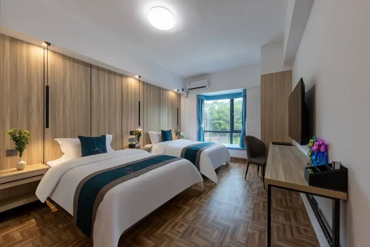 Ένα δωμάτιο ξενοδοχείου με δύο κρεβάτια, ένα γραφείο, μια καρέκλα, μια τηλεόραση και ένα παράθυρο με θέα σε καταπράσινο περιβάλλον.