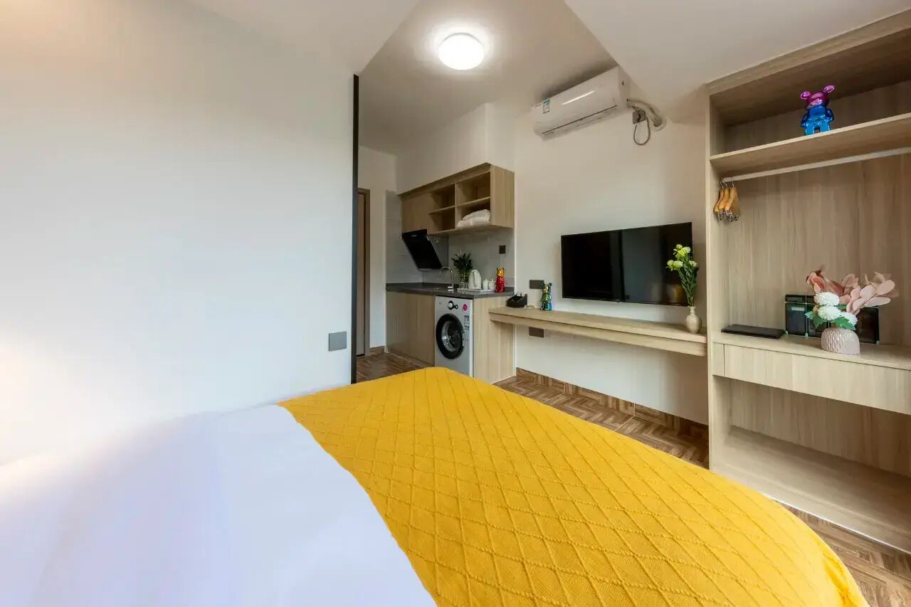 A compact room with a bed, a washing machine, a TV, and a small kitchenette.