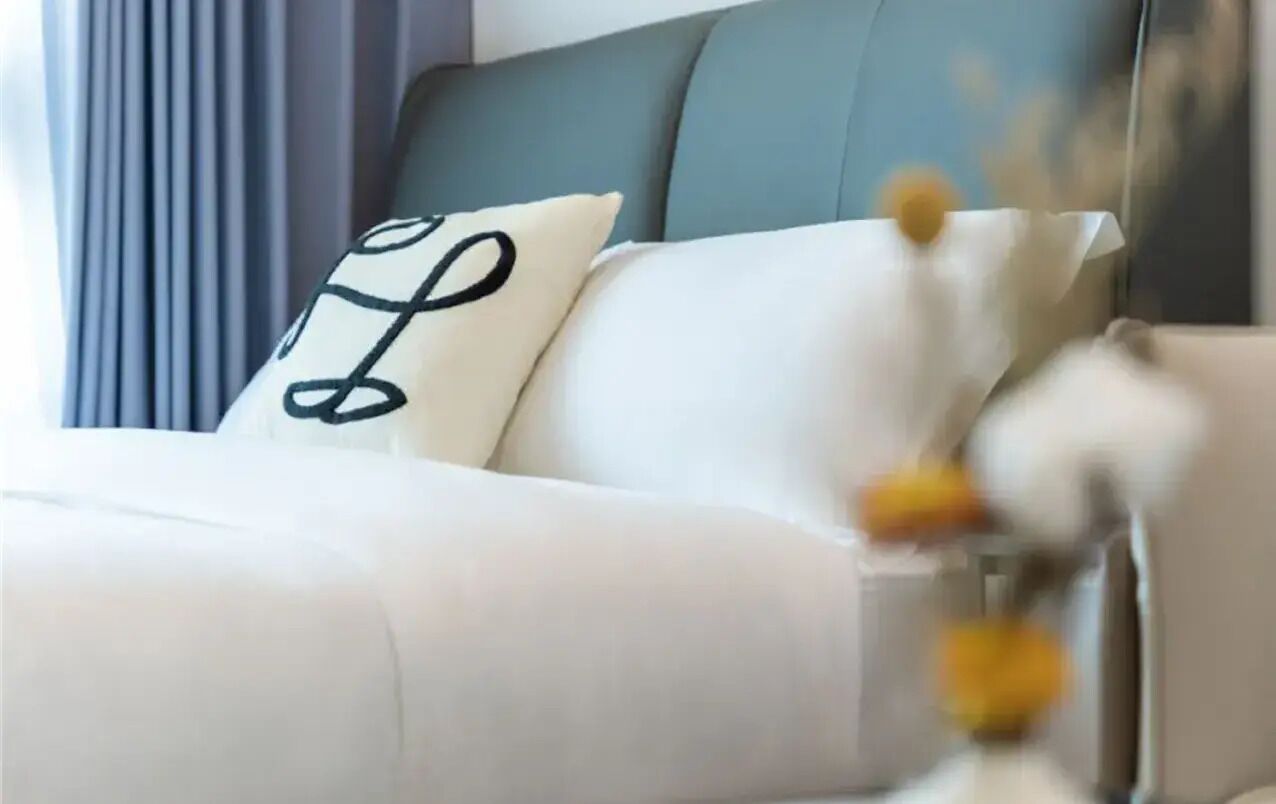 A bed with white bedding and a pillow with a black design.