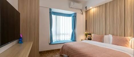 A hotel room with a bed, a TV, a window with curtains, and an air conditioning unit.