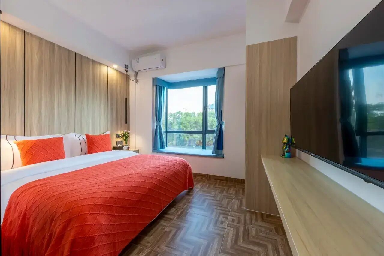 A hotel room with a bed, a TV, a window with curtains, and an air conditioning unit.