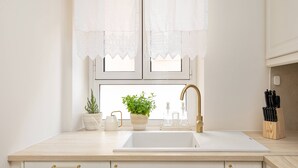 A kitchen with a white sink, a potted plant, a window with lace curtains, and a knife block. - Borgo Veneziano by Corfuescapes (Kerkira)