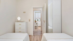 A bedroom with two beds, a dresser with a mirror, and a door leading to a kitchen area. - Borgo Veneziano by Corfuescapes (Kerkira)