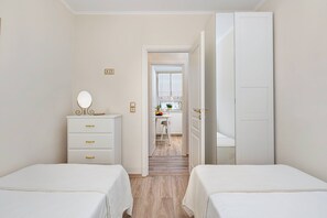 Ein Schlafzimmer mit zwei Betten, einer Kommode mit Spiegel und einer Tür zu einer Küchenzeile.