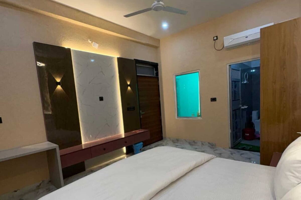 Un dormitorio con cama, ventilador de techo, aire acondicionado de pared y puerta que da a un baño.