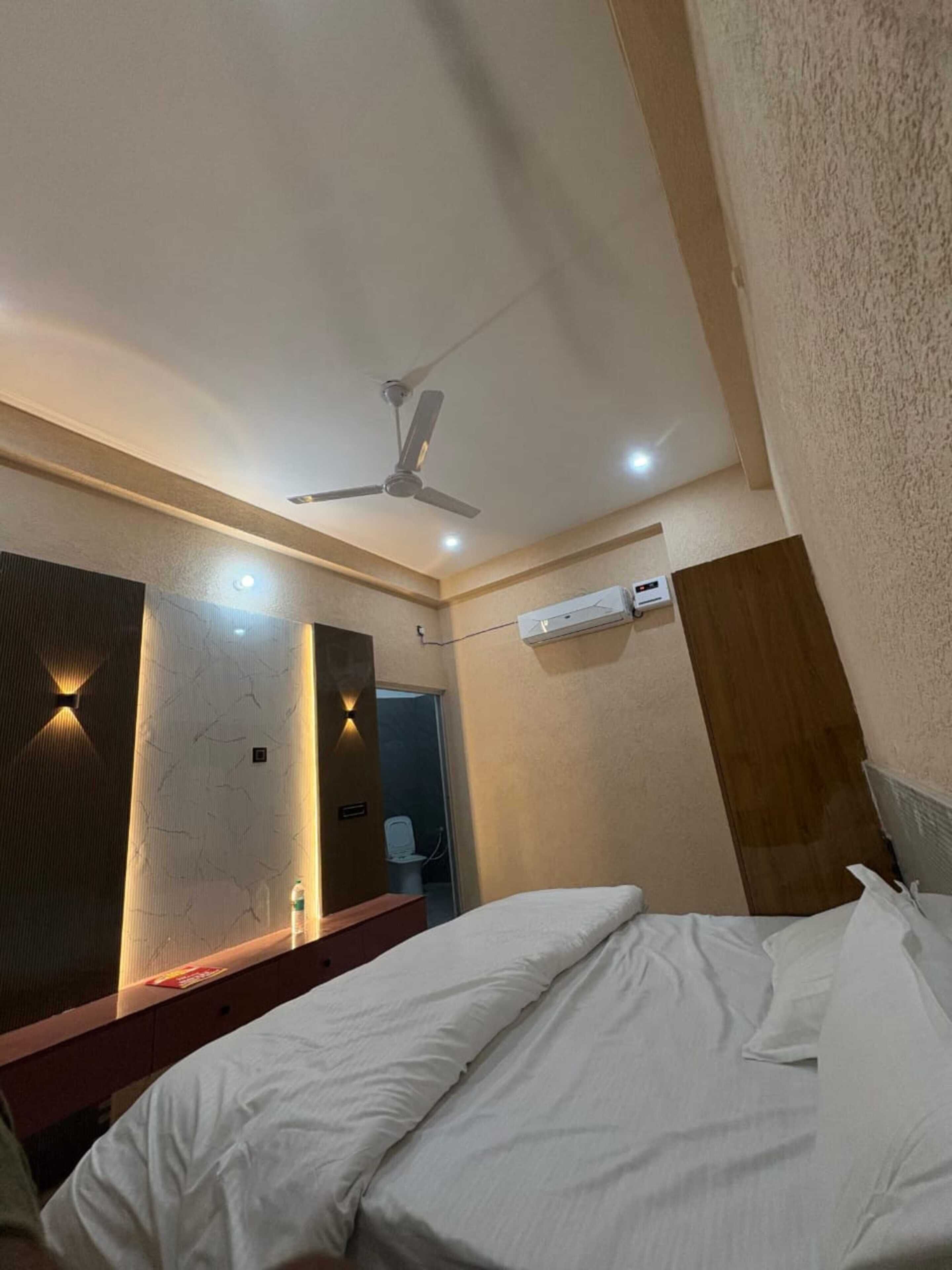 A hotel room with a bed, ceiling fan, air conditioning unit, and a bathroom visible through an open door.